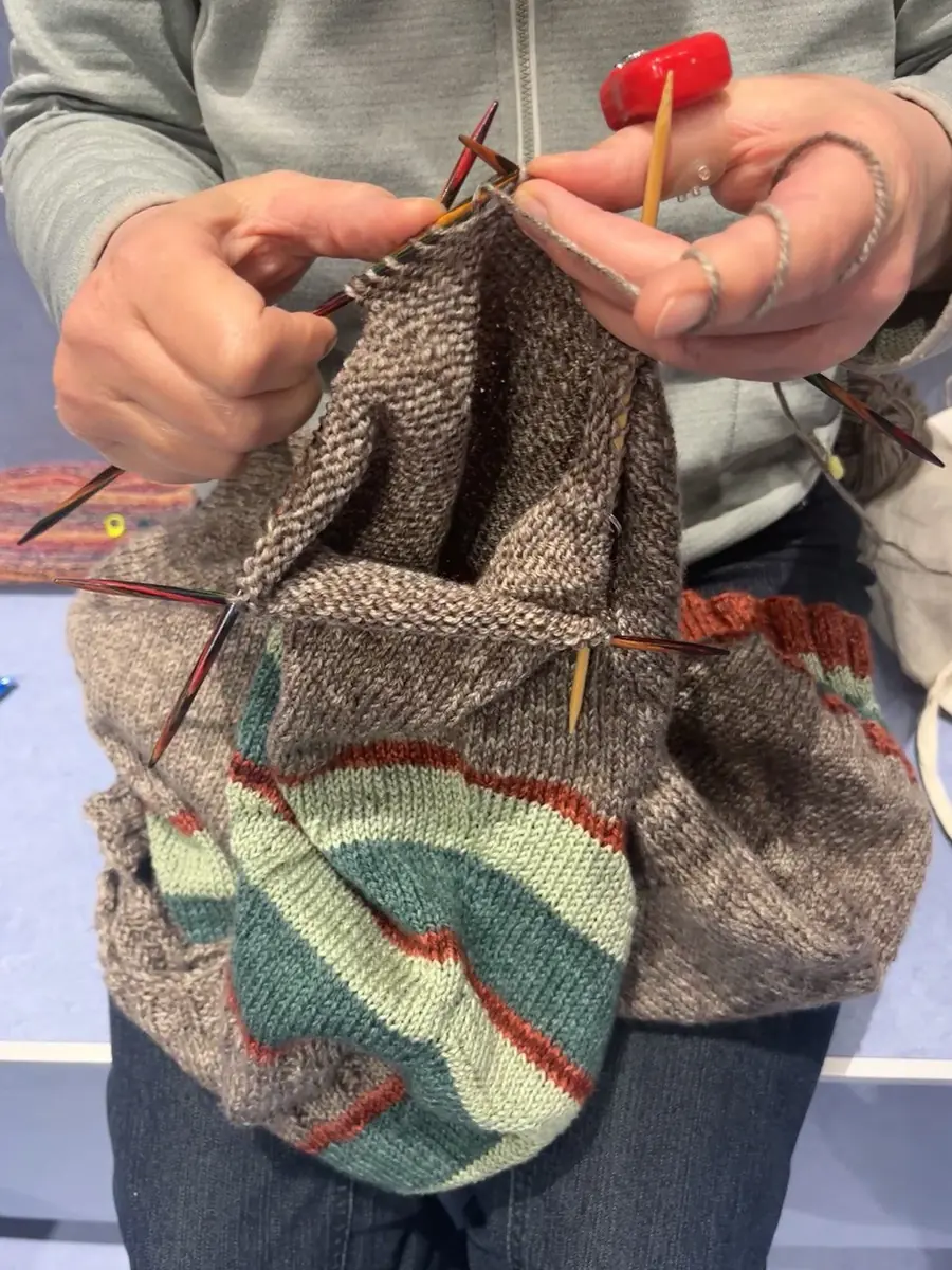 Zwei Hände stricken an einer mehrfarbig gestreiften Socke