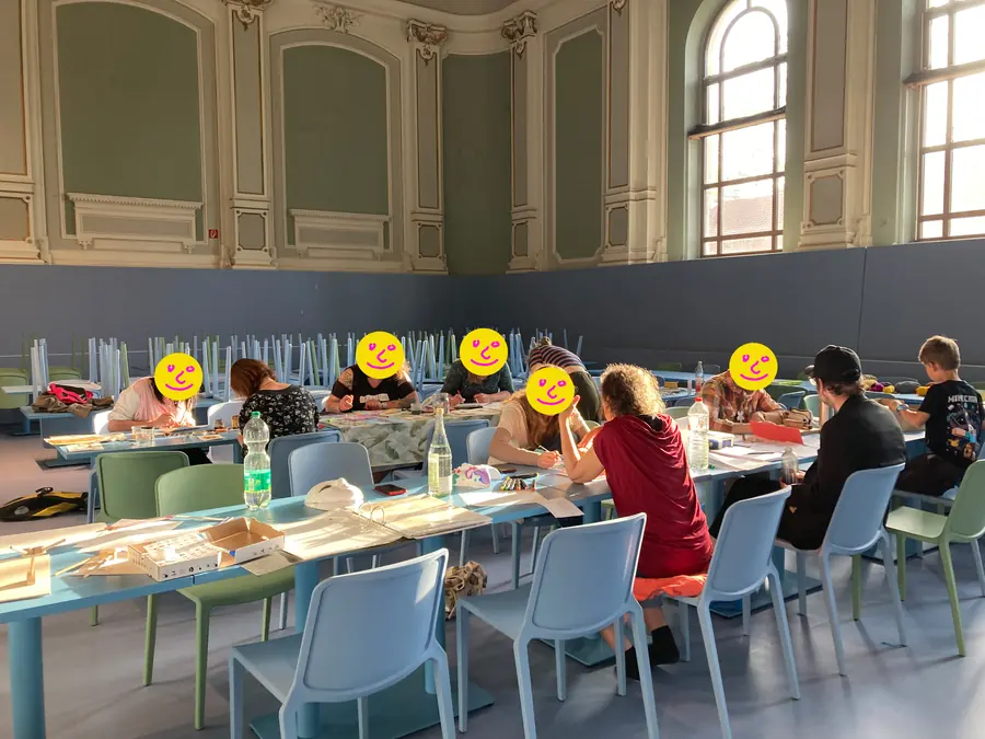Gruppe sitzt an einem langen Tisch im Saal und arbeitet an eigenen Projekten