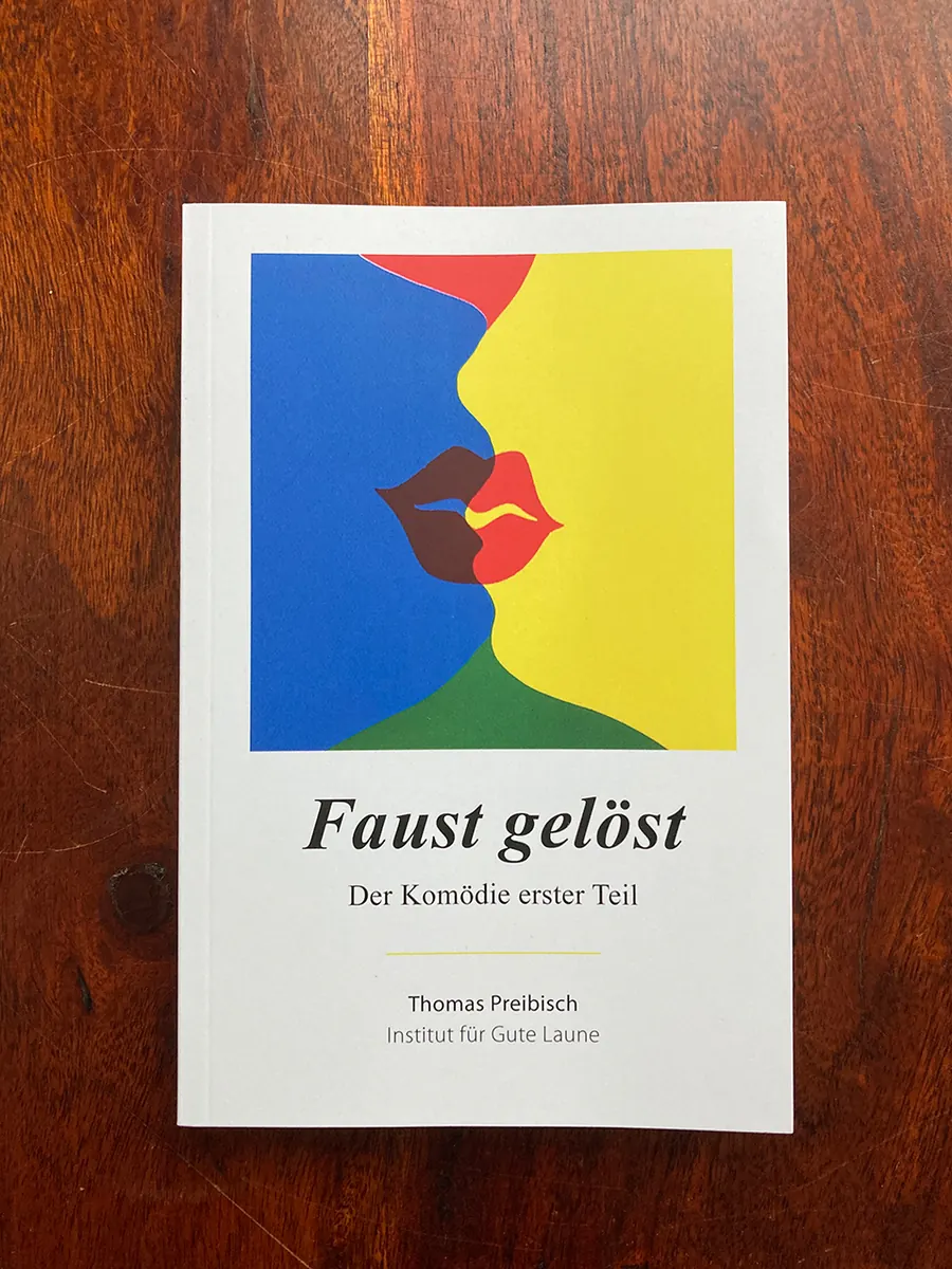 Das Buch „Faust gelöst“ auf einem Holztisch: zwei Gesichter im Profil in Blau und Gelb, die sich küssen