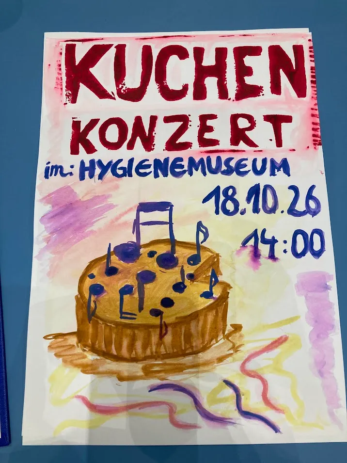 Handgemaltes Plakat: „Kuchenkonzert im Hygienemuseum, 18.10.26, 14:00“, darunter ein gemalter Kuchen, aus dem Notenschlüssel und Noten wachsen