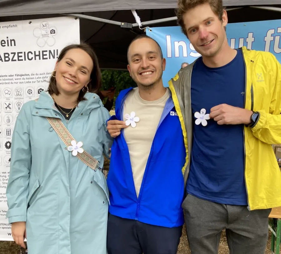 Drei Menschen zeigen auf ihre Kunstabzeichen