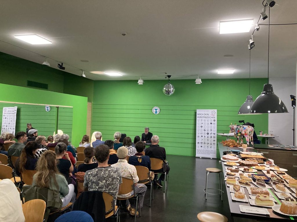 Voller Saal beim vierten Kuchenkonzert im Deutschen Hygiene-Museum Dresden, rechts der lange Kuchentisch